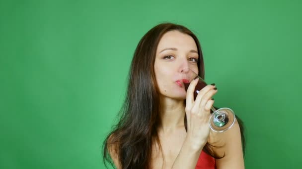 Une belle brune boit du vin dans un verre. Dégustation, choix, dépendance à l'alcool, fond vert — Video