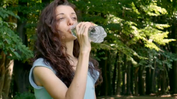 Al aire libre Retrato de la joven morena con el pelo rizado está bebiendo agua mineral en los árboles verdes Fondo . — Vídeo de stock