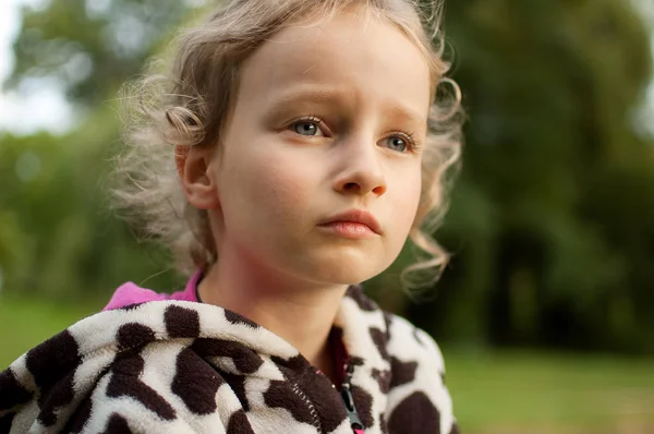 Retrato de una hermosa chica rizada de ojos azules sentada sobre un fondo de árboles verdes. Vacaciones en el pueblo . —  Fotos de Stock