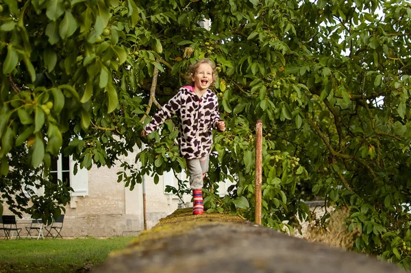 Dulce chica corriendo a lo largo de una cerca de piedra. Vacaciones en el campo, vacaciones en la naturaleza —  Fotos de Stock