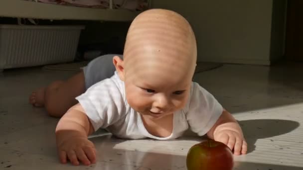 Bambino di sei mesi si trova sul pavimento e raggiunge per una mela rossa. Il bambino impara a strisciare. Bambino stanco e mettere la testa a terra — Video Stock