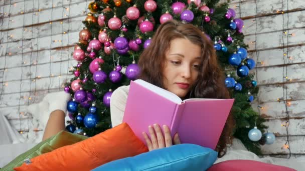 Joven morena está leyendo un libro sobre el fondo de un elegante árbol de Navidad. Colores no convencionales, decoraciones creativas para Navidad — Vídeo de stock