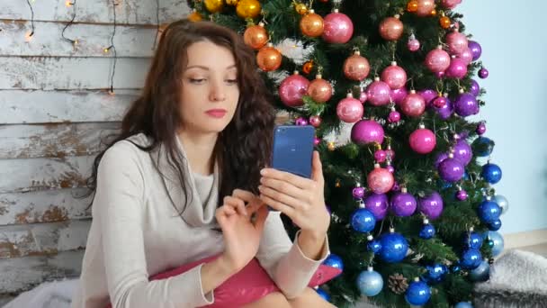 Різдвяна концепція - молода жінка фотографує селфі біля прикрашеної ялинки — стокове відео