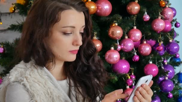 Jovem encaracolado falando em um telefone celular no fundo de uma árvore de Natal decorada criativamente — Vídeo de Stock