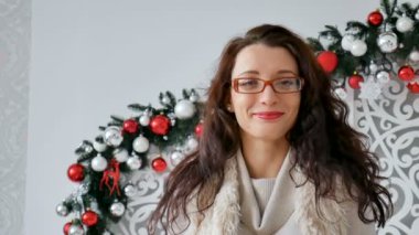 Gözlük ve sıcak kazak Noel dekor arka plan üzerinde giyen mutlu bir esmer kız portresi. Kıvırcık kız gülüyor