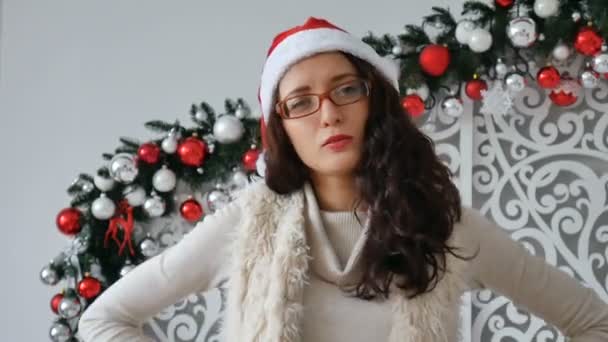 Mooie jongedame KERSTMUTS dragen over ingericht voor Kerstmis achtergrond met ernstige uitdrukking op het gezicht. Simpel en natuurlijk kijken naar de camera — Stockvideo