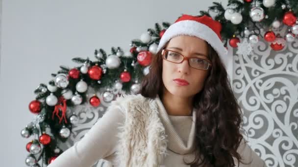 Young beautiful woman wearing christmas hat over decorated for christmas background with serious expression on face. Simple and natural looking at the camera — Stock Video