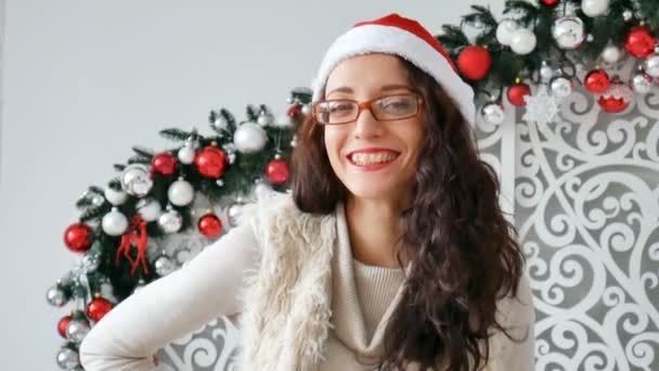 Beautiful young woman wearing santa claus hat and glasses for Chritmas celebration event. Attractive female being silly, making faces at dress up party. Background, close up, copy space — Stock Video