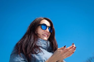 Açık havada yaşam tarzı karlı kış parkta yürüyüş güzel kız portresi kapatın. Gülümseyen ve kış zevk. Şık giyim güneş gözlüğü, mavi trençkot yansıtılmış