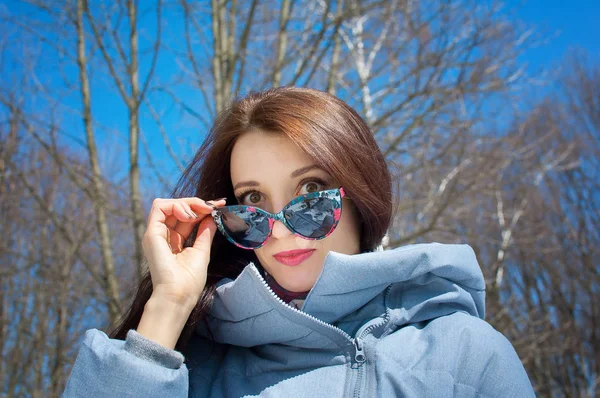 Våren porträtt. Vacker elegant flicka promenader i parken i solglasögon tidigt på våren på en solig dag — Stockfoto