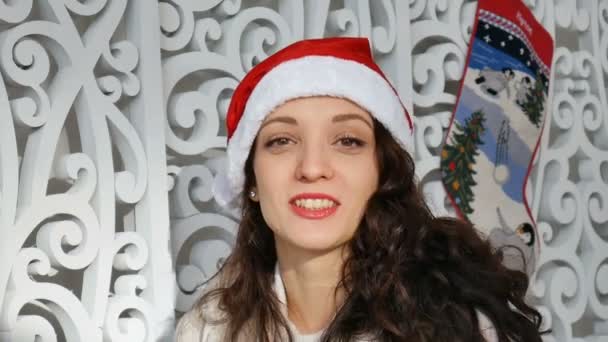 Concept de vacances et de personnes - belle femme sexy en chapeau de Père Noël et cheveux bouclés souriant dans le contexte de la décoration de Noël — Video