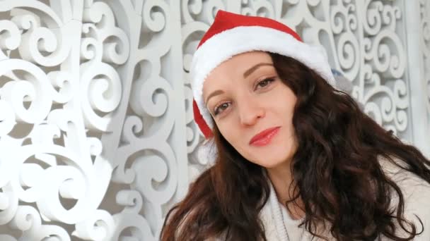Concept de vacances et de personnes - belle femme sexy en chapeau de Père Noël et cheveux bouclés souriant dans le contexte de la décoration de Noël — Video