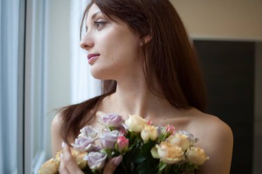 Bir buket çiçek ile yatak odası penceresinden bakarak güzel mutlu bir kadın. Bahar kavramı