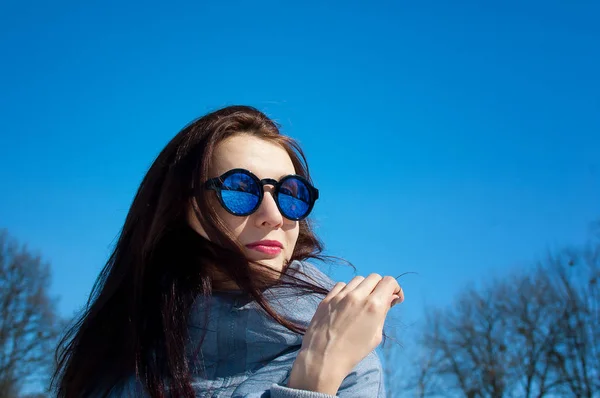 Draußen Nahaufnahme Porträt der schönen jungen Frau mit verspiegelter Sonnenbrille über blauem Himmel während des Vorfrühlings im Park. — Stockfoto