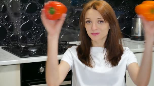 Unga brunett fru leker med röda och orange paprika som täcker hennes ögon med grönsaker innan du förbereder mat vid köket. Hälsosam livsstil och bantning koncept — Stockvideo