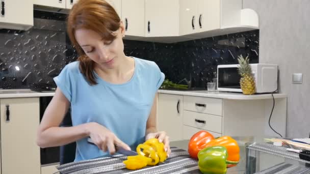 Mujer joven comiendo un trozo de pimiento amarillo mientras hace ensalada en la cocina. concepto de estilo de vida saludable . — Vídeos de Stock