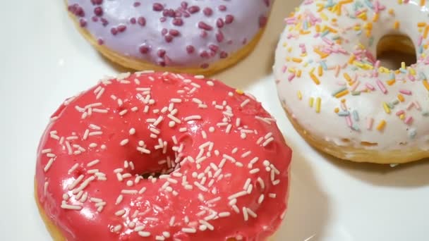 Donuts surtidos con espolvoreos de colores sobre plato blanco — Vídeo de stock