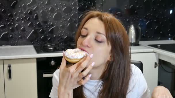 Mujer joven hambrienta comiendo donut en la cocina en casa. Concepto de comida sabrosa . — Vídeos de Stock