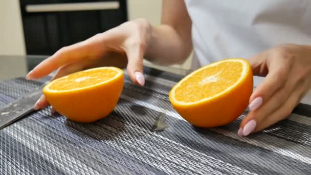 Руки женщины показывают две спелые сочные половинки апельсина на кухне дома — стоковое видео