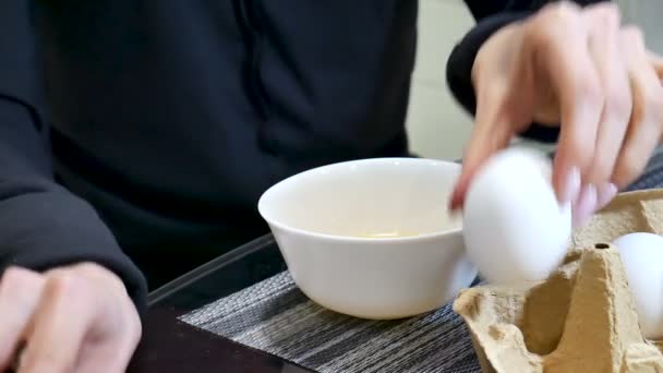 Manos de mujer rompiendo un huevo en un tazón de cerámica blanca en la cocina — Vídeos de Stock