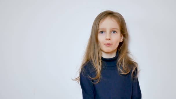 Videó az aranyos lány hosszú, szőke haja és grimaszok mellett a stúdióban, nagy kék szeme közelről — Stock videók