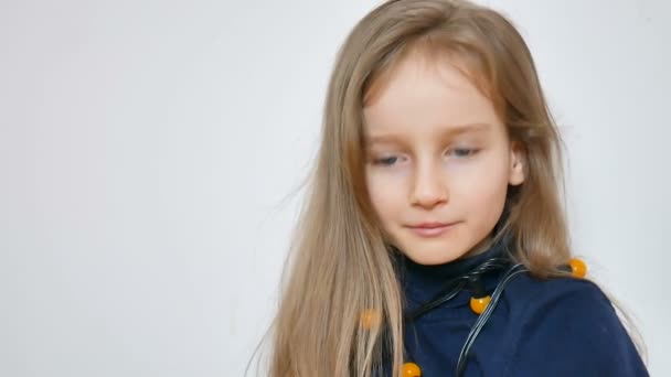 Indoors portrait of cute little girl with long blonde hair and big blue eyes wearing bunch of yellow Christmas lights on white background — Stock Video