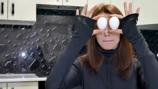 Close up video of young woman in black shirt covering her eyes with two chicken eggs. — Stock Video