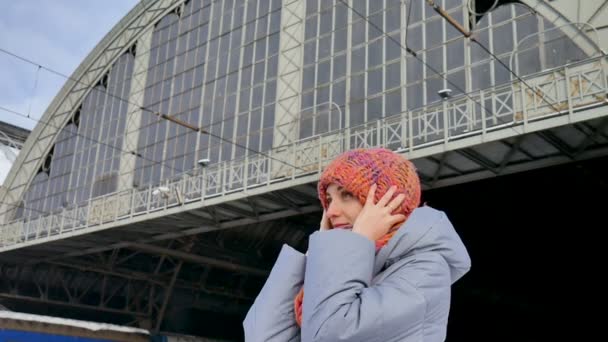 Attraente ragazza adulta in cappotto blu e cappello colorato in attesa di qualcuno alla stazione ferroviaria — Video Stock