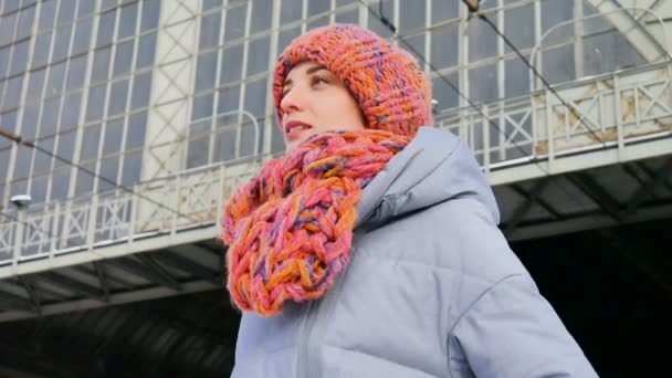 Close up ritratto invernale di una giovane donna in cappotto blu e cappello colorato alla stazione ferroviaria durante la soleggiata giornata fredda in attesa di un treno — Video Stock