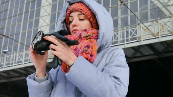 Vinter porträtt av en ung kvinna i blå kappa och färgglada hatt på stationen under solig kall dag. — Stockvideo