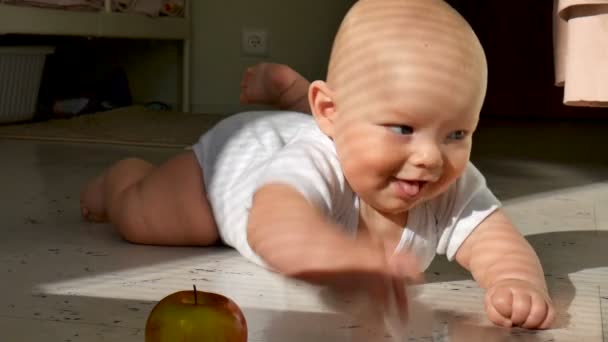 Χαμογελώντας μωρό προσπαθεί να πιάσει ένα μήλο στο πάτωμα — Αρχείο Βίντεο