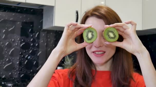 Jovem feliz animado brincando com kiwi maduro antes de preparar comida na cozinha. Emoções humanas positivas — Vídeo de Stock