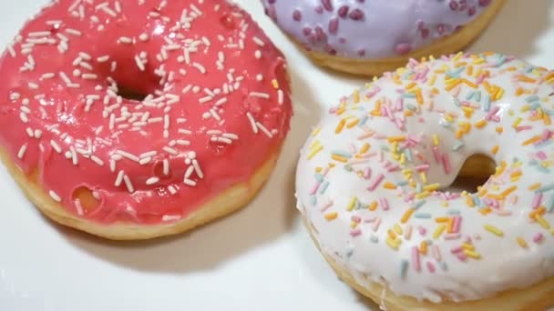 Vidéo rapprochée de beignets assortis avec des saupoudres colorées sur plaque blanche — Video