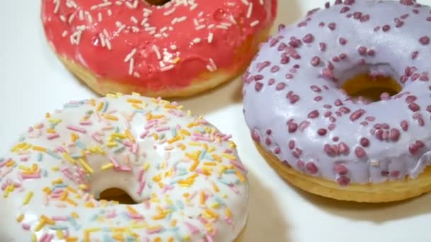 Close up vídeo de deliciosos donuts vermelhos, brancos e roxos com polvilhas coloridas na placa branca — Vídeo de Stock