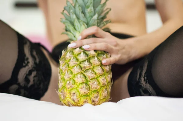 Foto van grote rijpe ananas tussen vrouwelijke benen in zwarte kousen — Stockfoto