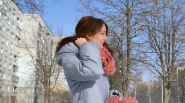 Çekici gülümseyen genç kadın mavi ceket ve şehirde erken Bahar zaman güneşli bir günde sırasında kameraya bakarak poz renkli örgü atkı