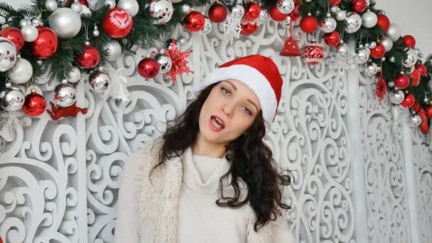 Retrato de hermosa joven morena en sombrero de santa rojo sonriendo y mirando a la cámara en el estudio — Vídeo de stock