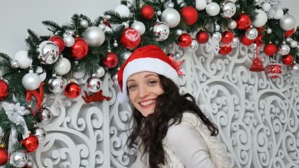 Freudig fröhliches Mädchen mit rotem Weihnachtsmann-Hut sendet einen Kuss in die Kamera im weihnachtlich dekorierten Studio — Stockvideo