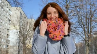 Açık havada gülümseyen genç kadın mavi ceket ve renkli portresi eşarp güneşli gün erken Bahar süre boyunca şehirde örme