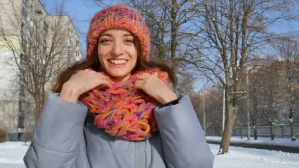 Portrait of smiling girl in warm coat and colorful knitted hat and scarf having fun outdoors during sunny day in spring on blue sky background — Stock Video