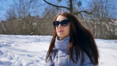 Siyah güneş gözlüğü ve düz saç genç kadın kışın güneşli ama soğuk gün sırasında sabahları parkta açık olmak zevk. Bahar konsepti bekleniyor.