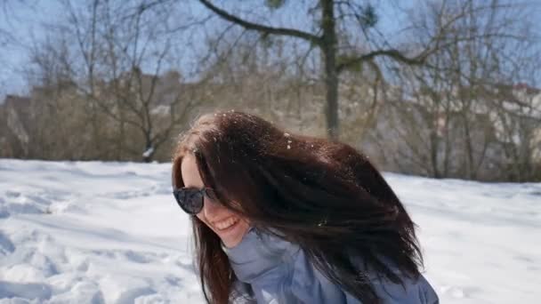 Portré vonzó nő fekete napszemüveg és egyenes Sötét haja játszik hógolyókat a szabadban a parkban, a reggeli napsütéses, de hideg nap. Téli játékkoncepció