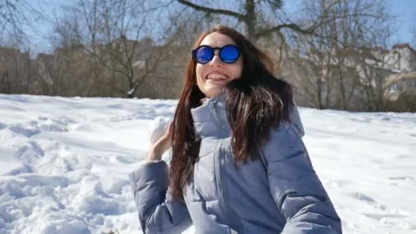 ブルーのミラー サングラスと春先に晴れているが寒い日には午前中に屋外の公園で誰かと遊ぶ雪玉を投げるストレート黒髪の美しい少女 — ストック動画