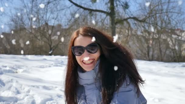 Outdoors female portrait of young active woman in dark sunglasses playing snowballs on blue sky background in the park — Stock Video