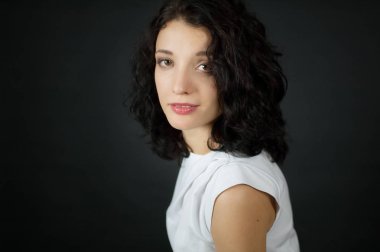 Siyah arka planda kamera instudio bakarak büyük gözleri ve kısa kıvırcık saçlı kadın yüz portre