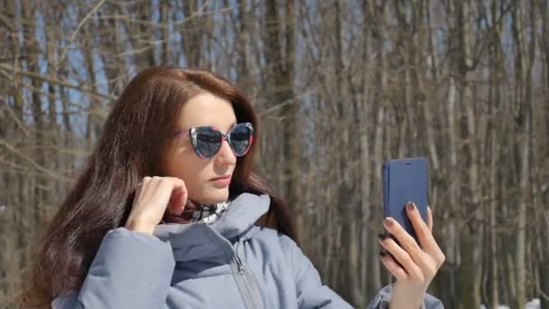 Kora tavasszal portréja fiatal nő vesz selfie szabadban a parkban a fák háttérben alatt napsütéses meleg nap — Stock videók