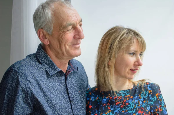 Pareja encantadora con diferencia de edad que mira aunque la ventana abierta dentro de la casa durante la primavera . —  Fotos de Stock