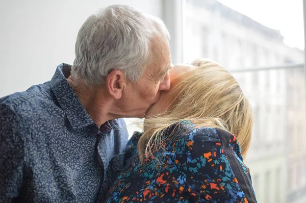 Caliente y sexy mujer de mediana edad disfrutando abrazo de su marido mayor de pie cerca de ventana abierta dentro de su casa. Pareja con diferencia de edad —  Fotos de Stock