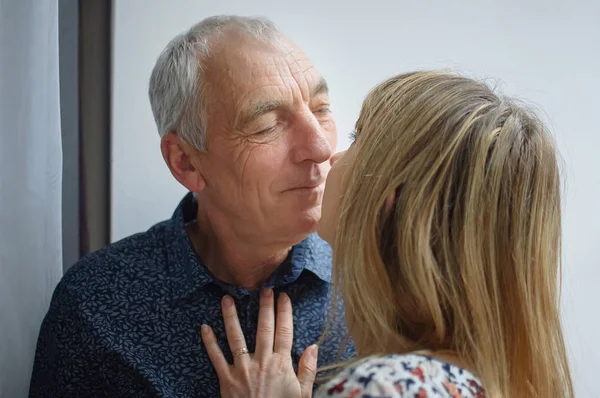 Caliente y sexy mujer de mediana edad besando a su marido anciano dentro de su casa. Pareja con diferencia de edad . —  Fotos de Stock