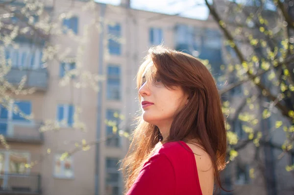 Jovem morena com lábios sensuais em camisa vermelha desfrutando de brisa da primavera ao ar livre, enquanto o sol está brilhando — Fotografia de Stock